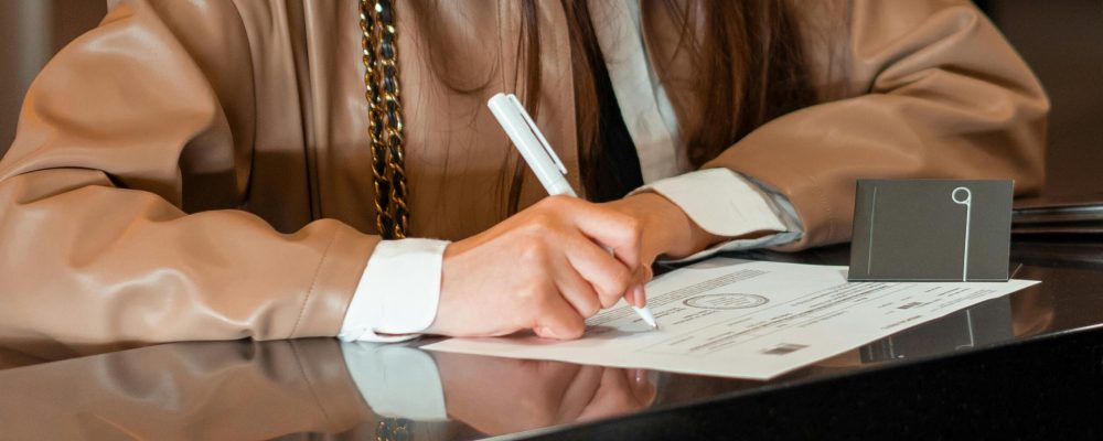 Close-up of a woman signing a document at a sleek reception counter, indoor setting.